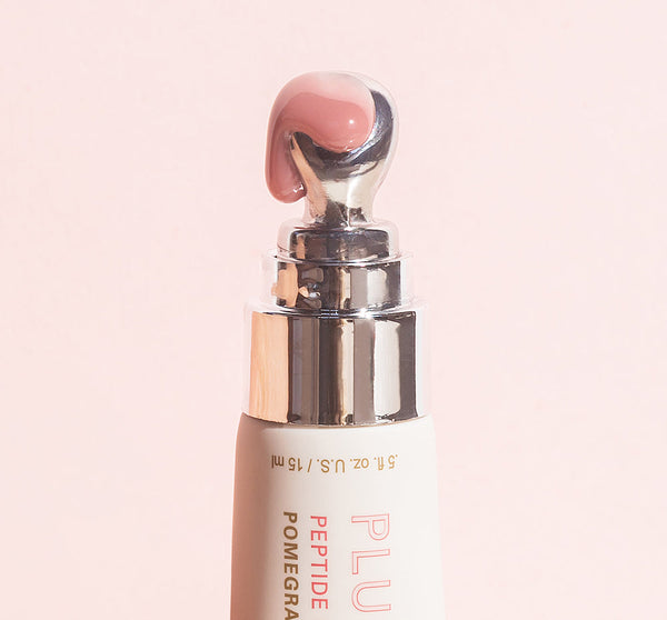 Close-up of a silver-tipped applicator releasing a soft pink balm from Plump Up Pretty Peptide Lip Treatment | Farmhouse Fresh against a pale pink background.