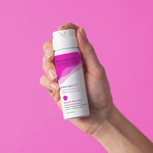 Hand holding a bottle of Preheels+ Blister Prevention Spray | Barefoot Scientist against a pink background, designed to protect and prevent blisters for comfortable wear.