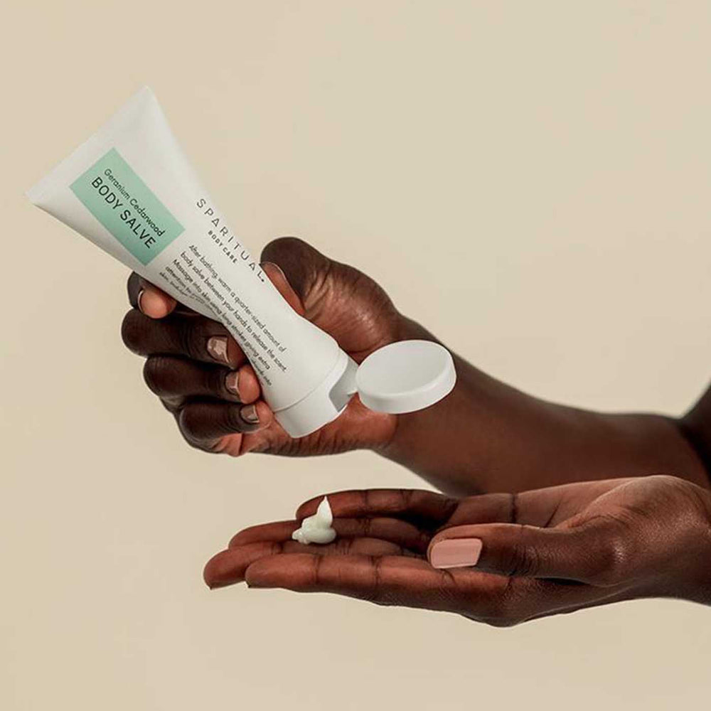 Person dispensing a small amount of Geranium Cedarwood BODY SALVE | Sparitual onto their palm, showcasing skincare and body care wellness.