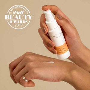 A person with neatly manicured nails holding a bottle of Citrus Cardamom HAND SERUM | Sparitual and dispensing the serum onto the back of their hand, showcasing skincare and body care product use.