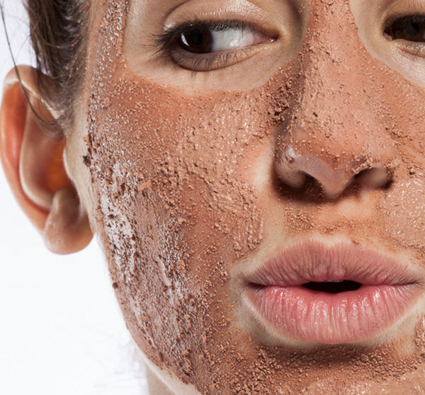 Close-up of a person with exfoliating sandy mud mask applied on their face, showcasing Sanded Ground® Clarifying Mud Exfoliation Mask | Farmhouse Fresh for skincare and gentle skin renewal.