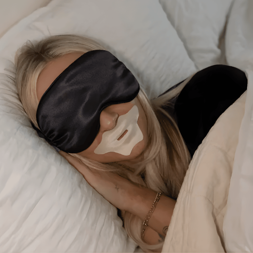 Woman sleeping wearing a black satin eye mask and Mouth Tape | Seald™ Wellness applied on her lips, promoting restful sleep and wellness.