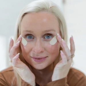 Woman with light skin and blonde hair applying Face Tape Smoothing Strips | Seald™ Wellness under her eyes, demonstrating a skincare and wellness routine.