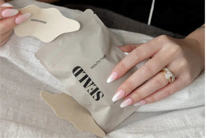 Hand holding a beige packet labeled Mouth Tape | Seald™ Wellness with adhesive strips designed for mouth taping laid on a soft fabric surface.