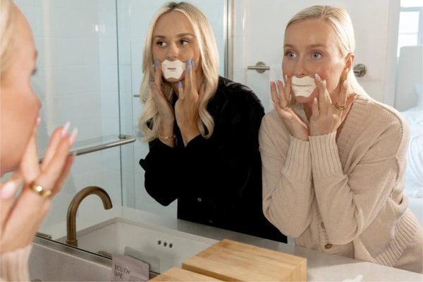 Woman applying Mouth Tape | Seald™ Wellness in front of a bathroom mirror, demonstrating its use as a wellness device to promote better breathing and sleep quality.