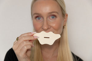 Woman holding a beige lip-shaped Mouth Tape | Seald™ Wellness product near her face, promoting wellness and nighttime breathing support.