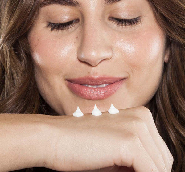 Close-up of a woman with smooth skin smiling gently as she applies three small dollops of cream on her hand, promoting Skin Saviors Shea Butter Sampler | Farmhouse Fresh skincare.