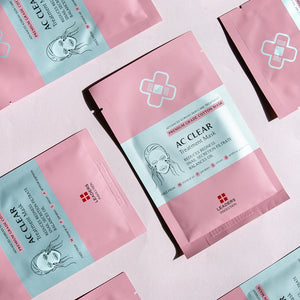 Several pink packets of AC Clear Skin Clinic Mask | Leaders with white and red text, displayed on a light pink background, featuring skincare treatment information on the packaging.