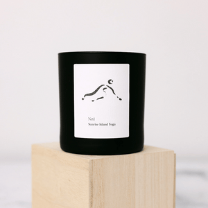 Minimalist black candle with a simple abstract figure on the label, placed on a light wooden block, featuring the No. 1 Sunrise Island Yoga (Bali) Candle | Lucky Owl product.