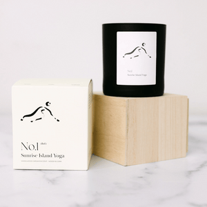 Minimalist black candle labeled No. 1 Sunrise Island Yoga (Bali) Candle | Lucky Owl next to its white packaging box on a wooden block and marble surface.
