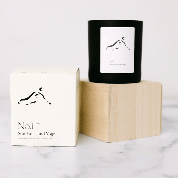 Minimalist black candle labeled No. 1 Sunrise Island Yoga (Bali) Candle | Lucky Owl next to its white packaging box on a wooden block and marble surface.