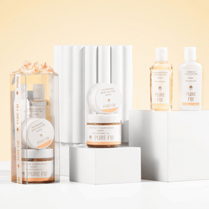 Spa Glow Box | Pure Fiji featuring nourishing body butter, coconut sugar scrub, exotic coconut oil, and hydrating body lotion displayed on white pedestals with a soft beige background.