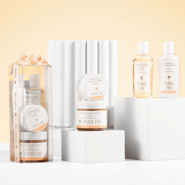 Spa Glow Box | Pure Fiji featuring nourishing body butter, coconut sugar scrub, exotic coconut oil, and hydrating body lotion displayed on white pedestals with a soft beige background.