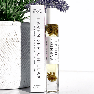 Lavender Chillax Organic Perfume Roll-on | Hydra Bloom featuring clear glass bottle with visible lavender buds and white cap beside white box packaging, placed near green plant.