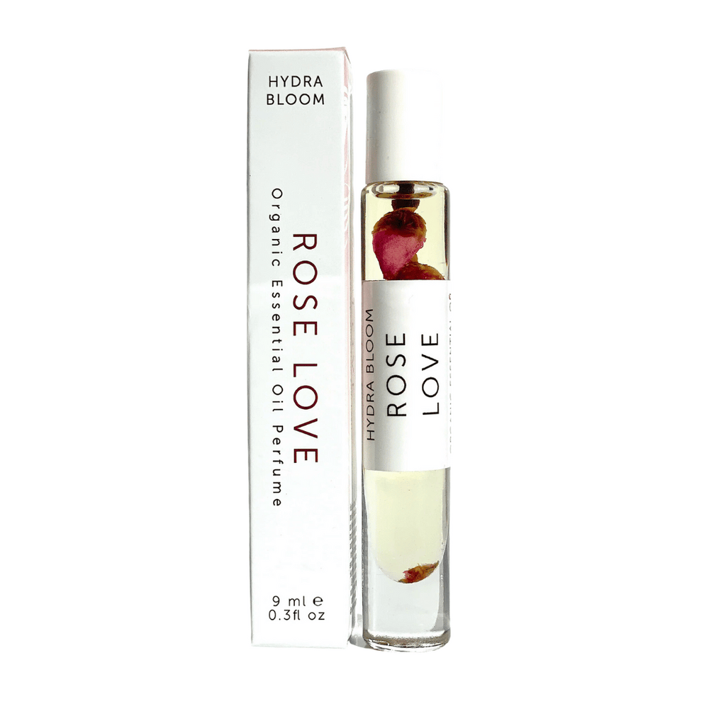 Rose Love Organic Perfume Roll-on | Hydra Bloom with a clear glass bottle containing oil and rose petals, displayed next to its white packaging for skincare and wellness use.