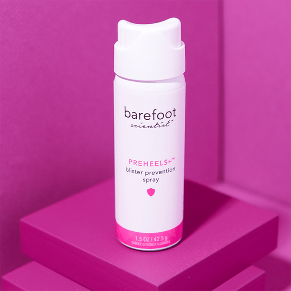 Preheels+ Blister Prevention Spray | Barefoot Scientist in a white bottle with pink accents, displayed on pink geometric platforms, promoting skincare and body care for foot comfort.