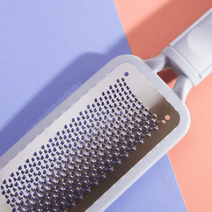 Close-up of the stainless steel grating surface and white handle of The Gratest Professional Micro-Grated XL Rasp | Barefoot Scientist against a pastel blue and peach background.