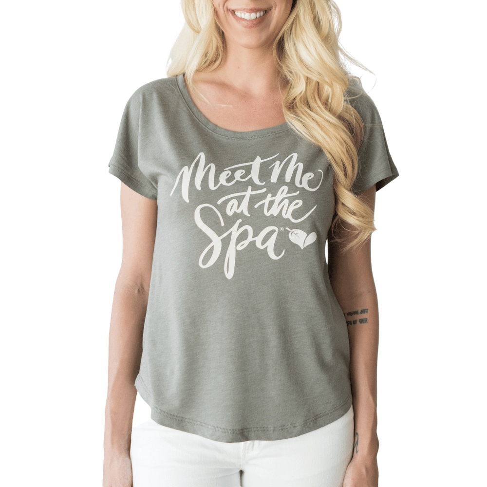 Woman wearing a soft gray Meet Me at the Spa Calligraphy Women's T-Shirt | Lucky Owl with white script text, paired with white pants, smiling with long blonde hair.