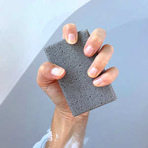 Hand holding the In The Buff Dual-Texture Siliglass Pumice Stone | Barefoot Scientist above water, showcasing its textured surface for effective skincare and body care exfoliation.