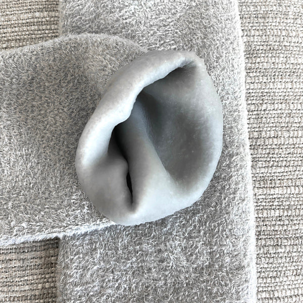 Close-up of soft, plush gray Sleep On It Overnight Moisturizing Gel Socks | Barefoot Scientist resting on a textured fabric surface, highlighting the smooth gel interior for skincare and body care wellness.