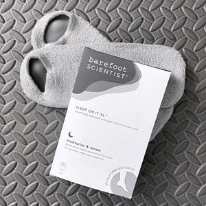 Sleep On It Overnight Moisturizing Gel Socks | Barefoot Scientist packaging displayed on gray textured surface with a pair of soft gray open-toe gel socks underneath.