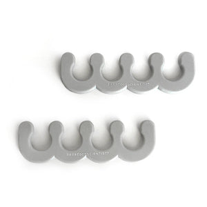 Two gray silicone toe separators designed for pedicure use, each featuring a curved, wavy shape with the text "barefoot SCIENTIST" printed on them, part of the Spaced Out | Barefoot Scientist collection.
