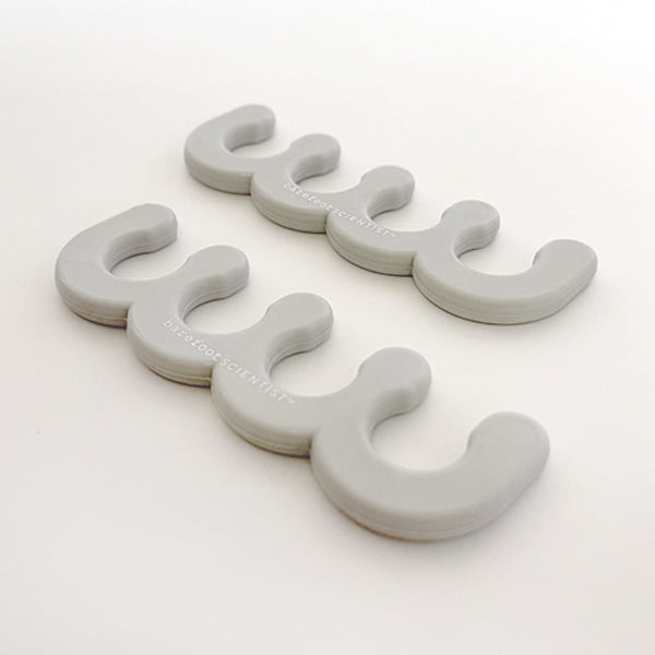 Two pairs of gray silicone toe separators for pedicures, branded with Spaced Out | Barefoot Scientist, designed to promote foot wellness and comfort.