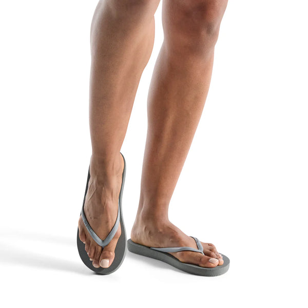 Woman wearing grey and black Slimz Core Sandals | Feelgoodz standing on a white background with a relaxed posture.