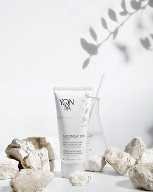 GlycoNight 10% Peel Masque | Yon-Ka Paris tube displayed among white natural stones next to a glass beaker with a clear stirring rod, conveying a clean skincare and wellness aesthetic.