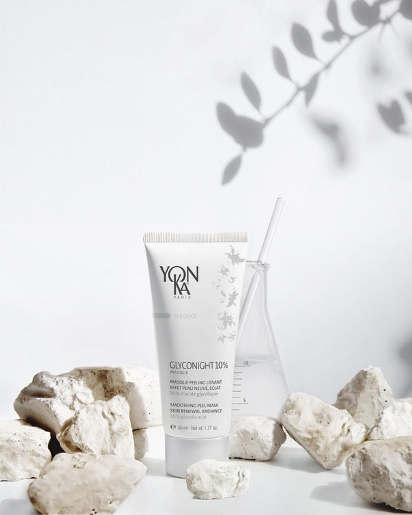 GlycoNight 10% Peel Masque | Yon-Ka Paris tube displayed among white natural stones next to a glass beaker with a clear stirring rod, conveying a clean skincare and wellness aesthetic.