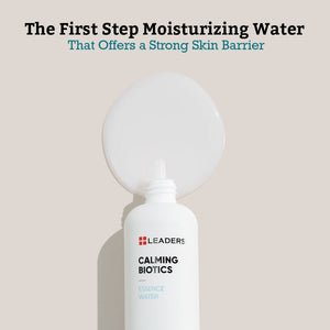 White bottle of Calming Biotics Essence Water | Leaders with clear moisturizing water spilled behind it on a beige background, highlighting its role in strengthening the skin barrier.