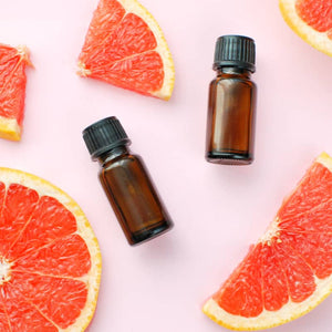 Two small amber glass bottles with black caps surrounded by fresh grapefruit slices, representing the skincare product Clarifying Face & Body Oil | Privai.