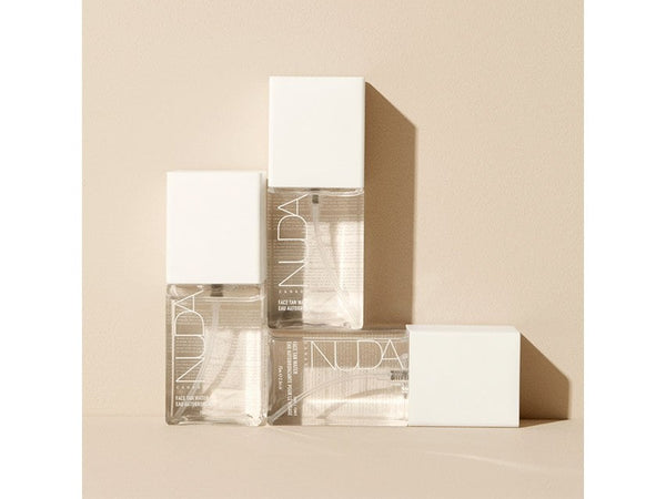 Three clear bottles of Face Tan Water - Dark | NUDA with white caps arranged on a beige surface, showcasing minimalist skincare packaging.
