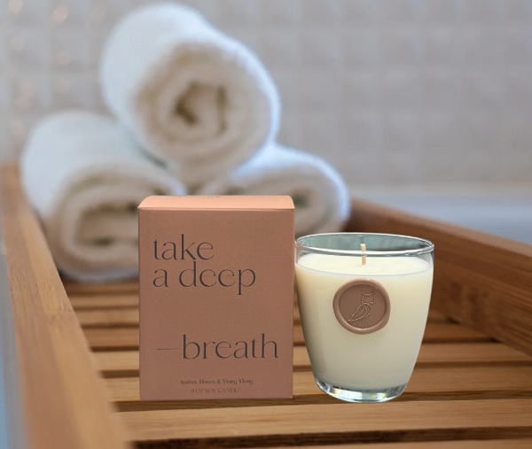 Luxe Bath Ritual Kit | Live Love Spa featuring a scented candle with amber, honey, and ylang ylang notes beside rolled white towels on a wooden bath tray.