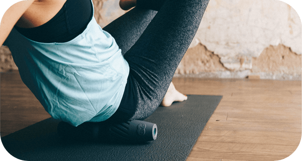 Person using a black RAD HELIX | RAD foam roller on a yoga mat for recovery and muscle relief in a wellness setting.