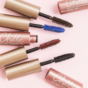 Four open tubes of Good Drama Mascara | Chella in various shades including blue, brown, burgundy, and black, arranged on a light pink background.