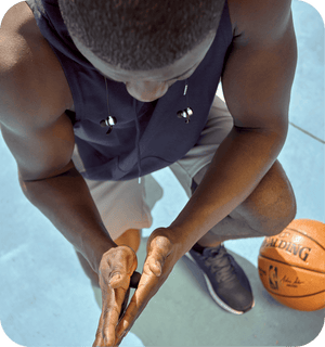 Athlete wearing headphones uses Micro Rounds | RAD wellness device on hands during basketball practice for recovery and body care outdoors.