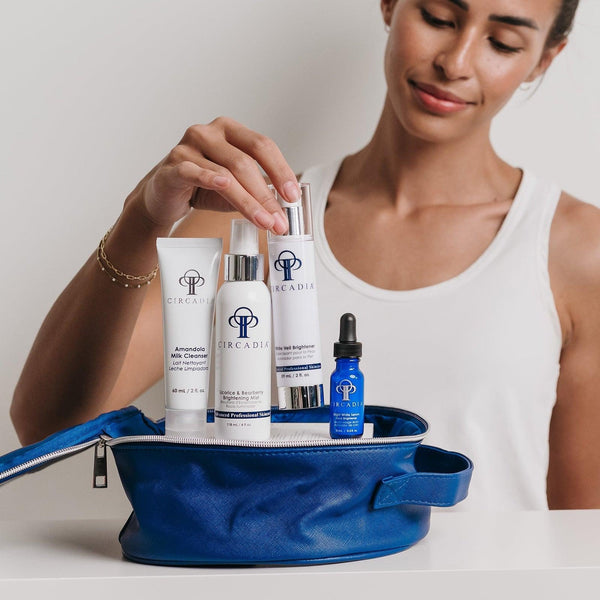 Woman holding skincare product from Pigmentation Regimen Bundle | Circadia with additional products arranged in a blue cosmetic bag on a white surface