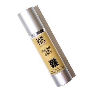 Brightening Cream Cleanser | Kindness Powered Skincare in a sleek silver bottle casting a soft shadow, emphasizing its creamy yellow formula for skincare wellness.