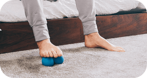 Person using blue massage tool on foot while seated, demonstrating recovery and wellness with RAD Roller Original | RAD for body care and muscle relief.