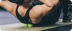 Person using green massage balls under upper back on a yoga mat for muscle release and recovery with the RAD Roller Original | RAD.