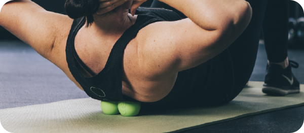 Person using a RAD Roller Stiff | RAD massage roller with two green balls on an exercise mat for muscle recovery and wellness.