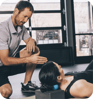 Man demonstrating use of RAD Roller Stiff | RAD as a recovery tool by applying it to a woman's neck for muscle relief in a wellness setting.