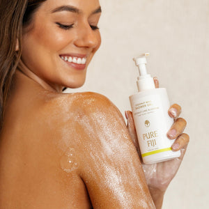 Smiling woman with wet skin holding a bottle of Coconut Milk Shower Gel | Pure Fiji, showcasing skincare and body care for a refreshing, nourishing shower experience.