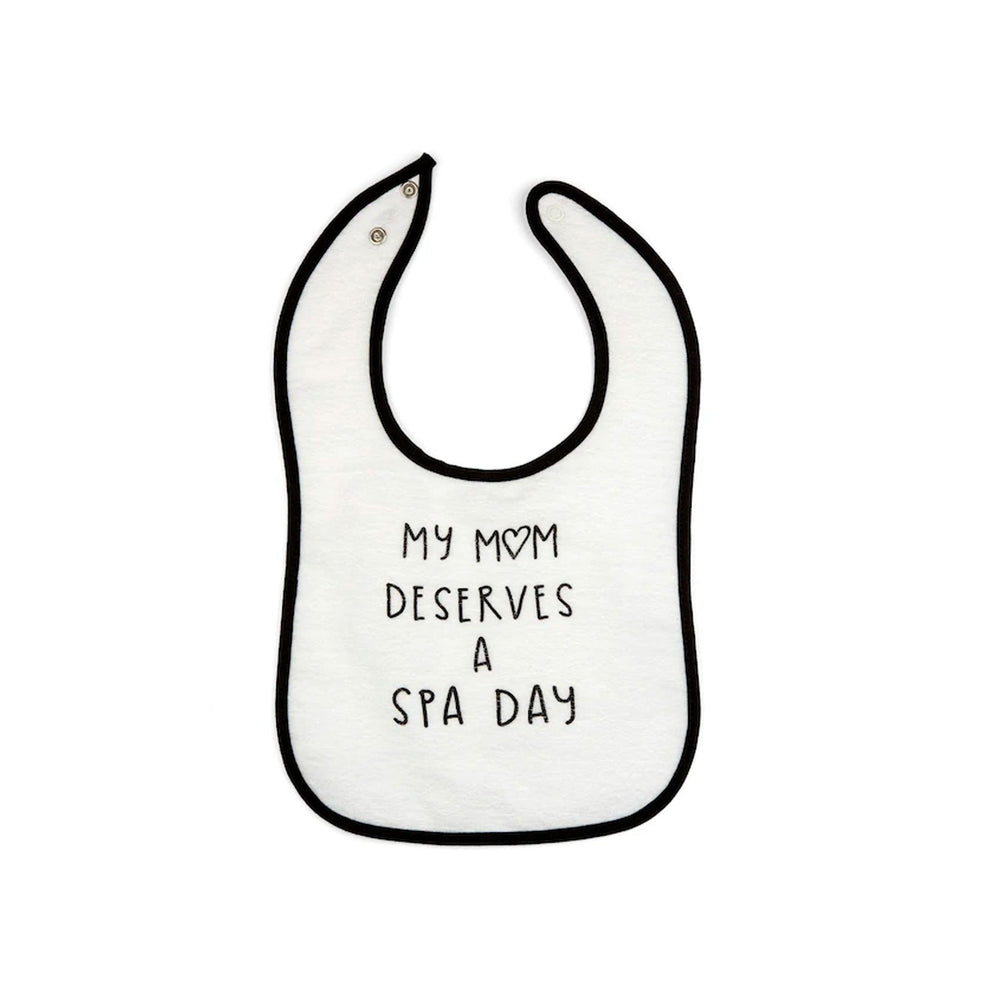 White baby bib with black trim and the phrase "My mom deserves a spa day" printed in simple black lettering, featuring the product name Mom Deserves A Spa Day Baby Bib | Lucky Owl.