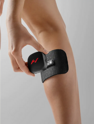 Close-up of a person applying the Venom Go | Hyperice, a black textured wellness device, to the back of their leg for muscle recovery and pain relief.